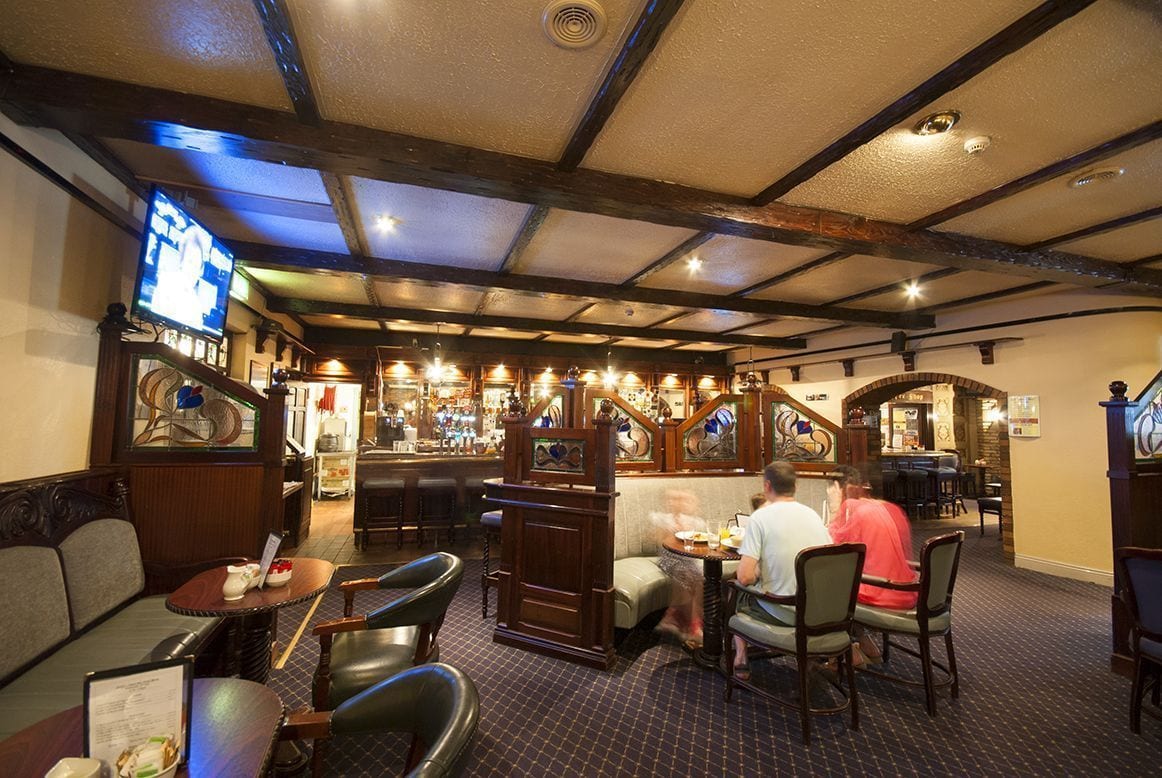 A restaurant with wooden furniture, a bar area, and a television screen.