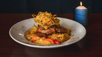 A plate of food with noodles, meat, and vegetables, accompanied by a lit candle and a blue candle holder.