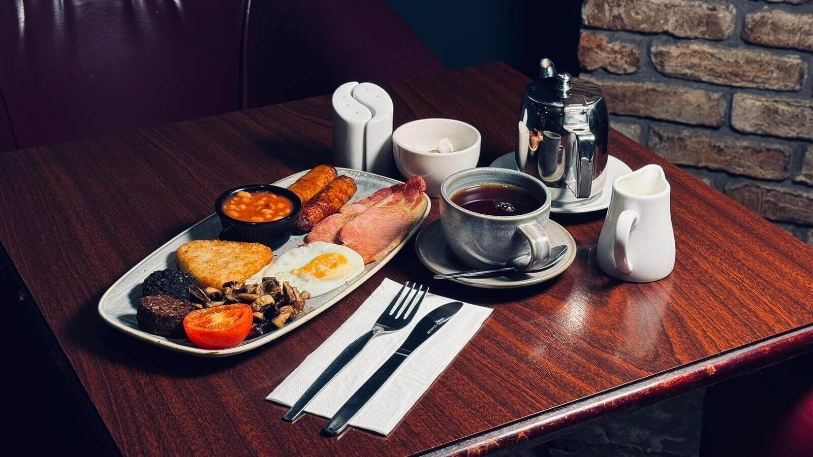 Un plateau de petit-déjeuner avec des œufs, des saucisses, des haricots, des toasts et une tasse de café, posé sur une table en bois.