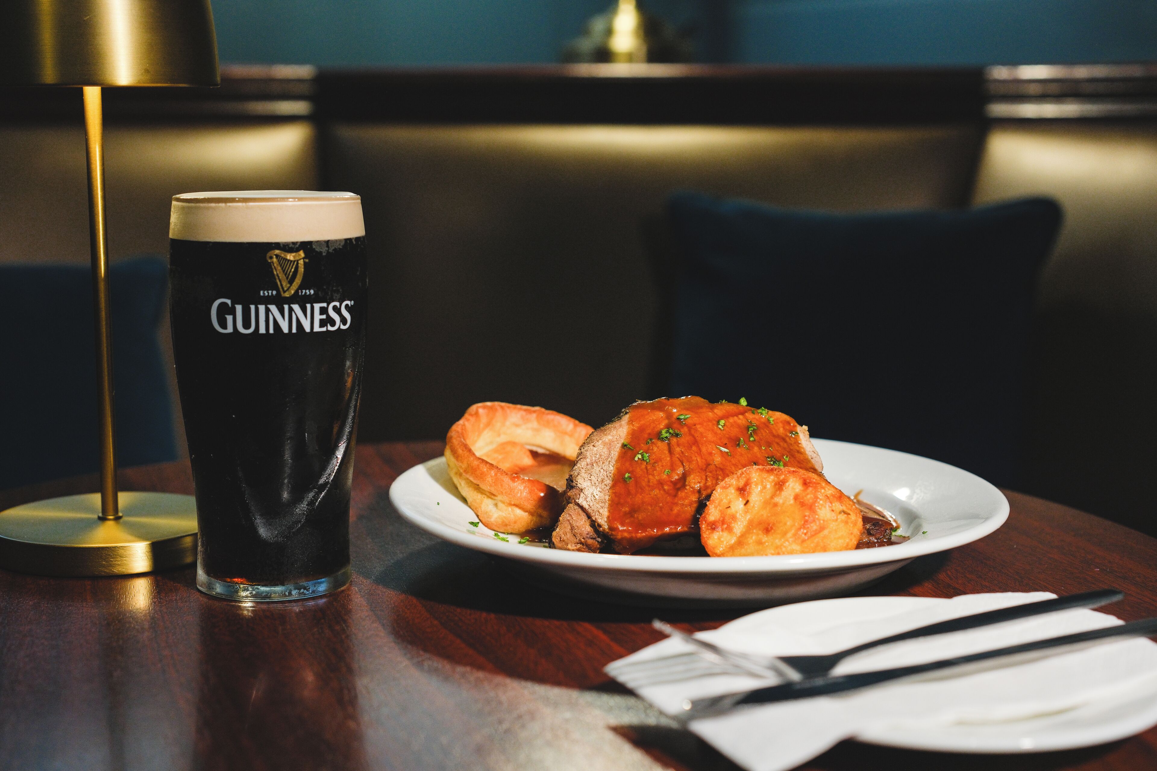 Una mesa con un vaso de cerveza Guinness, un plato de comida y cubiertos.
