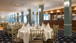 A formal dining room with round tables, gold chairs, and a bar area in the background. - Dooly's Hotel  (Birr)