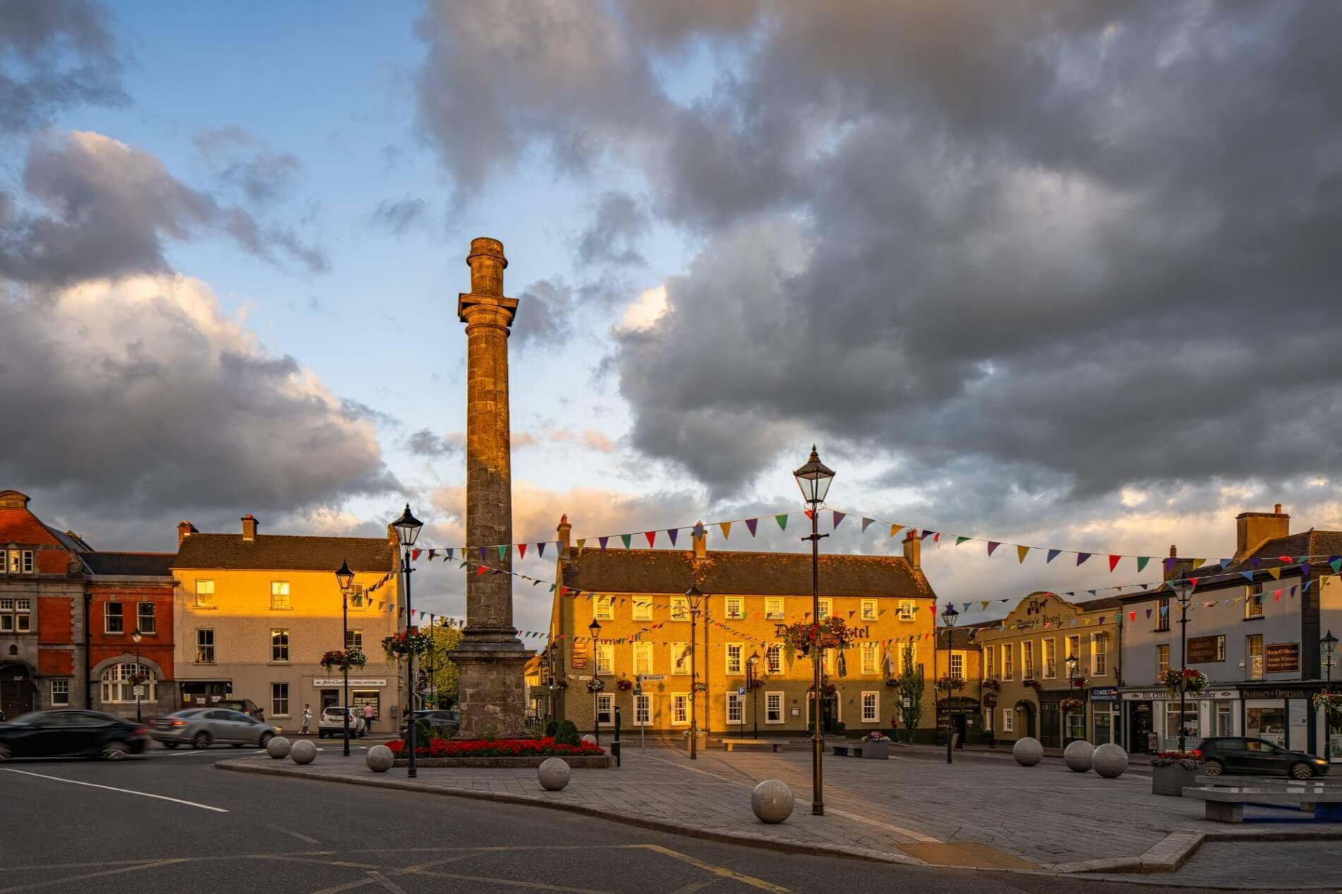 A historic square with a prominent stone obelisk, surrounded by traditional buildings with warm lighting.