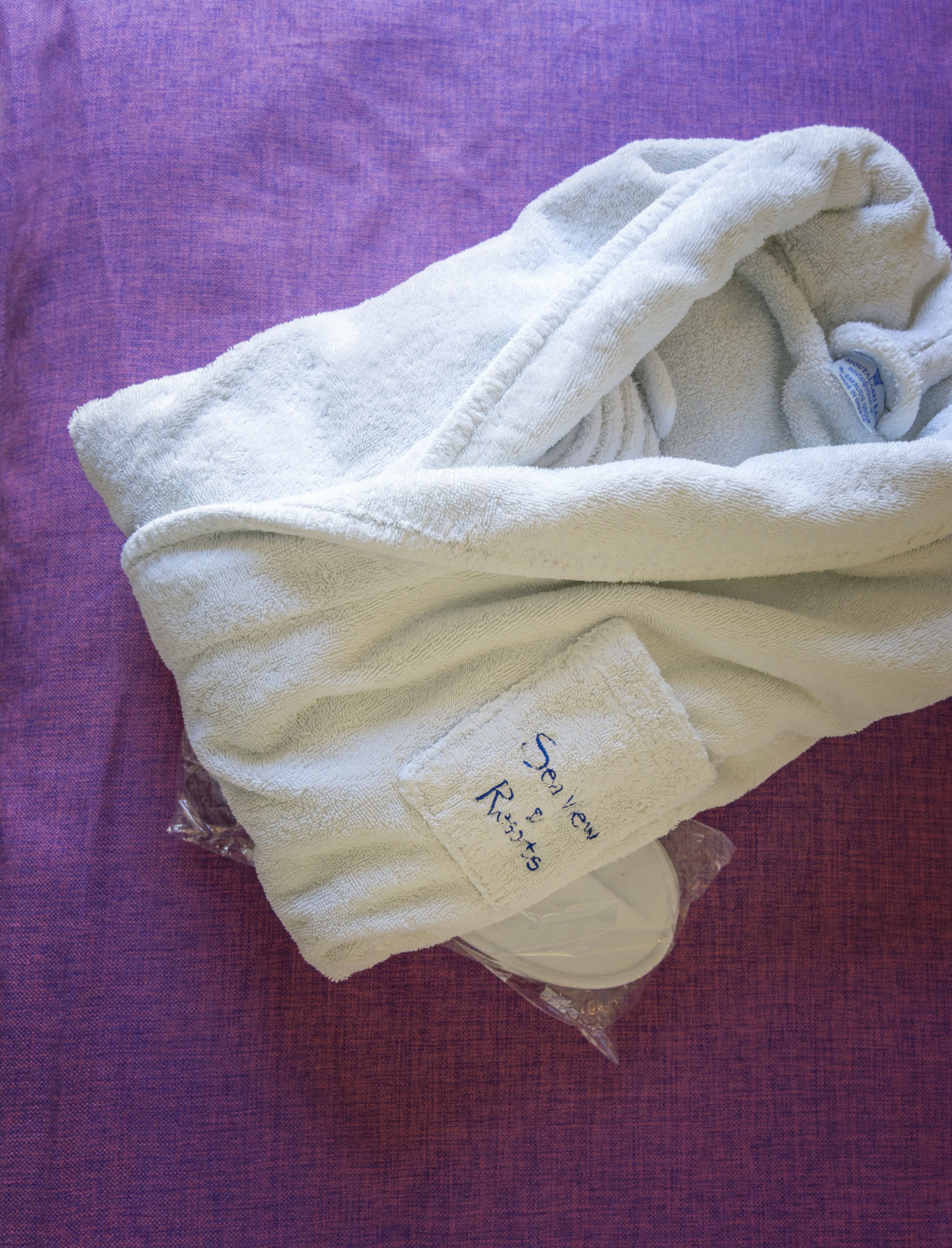A folded white towel with embroidered text on it, placed on a purple fabric surface.