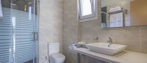 Un baño moderno con cabina de ducha de vidrio, inodoro, lavabo con espejo y toallero con toallas dobladas.