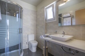 A modern bathroom with a glass shower enclosure, a toilet, a sink with a mirror above it, and a towel rack with folded towels.