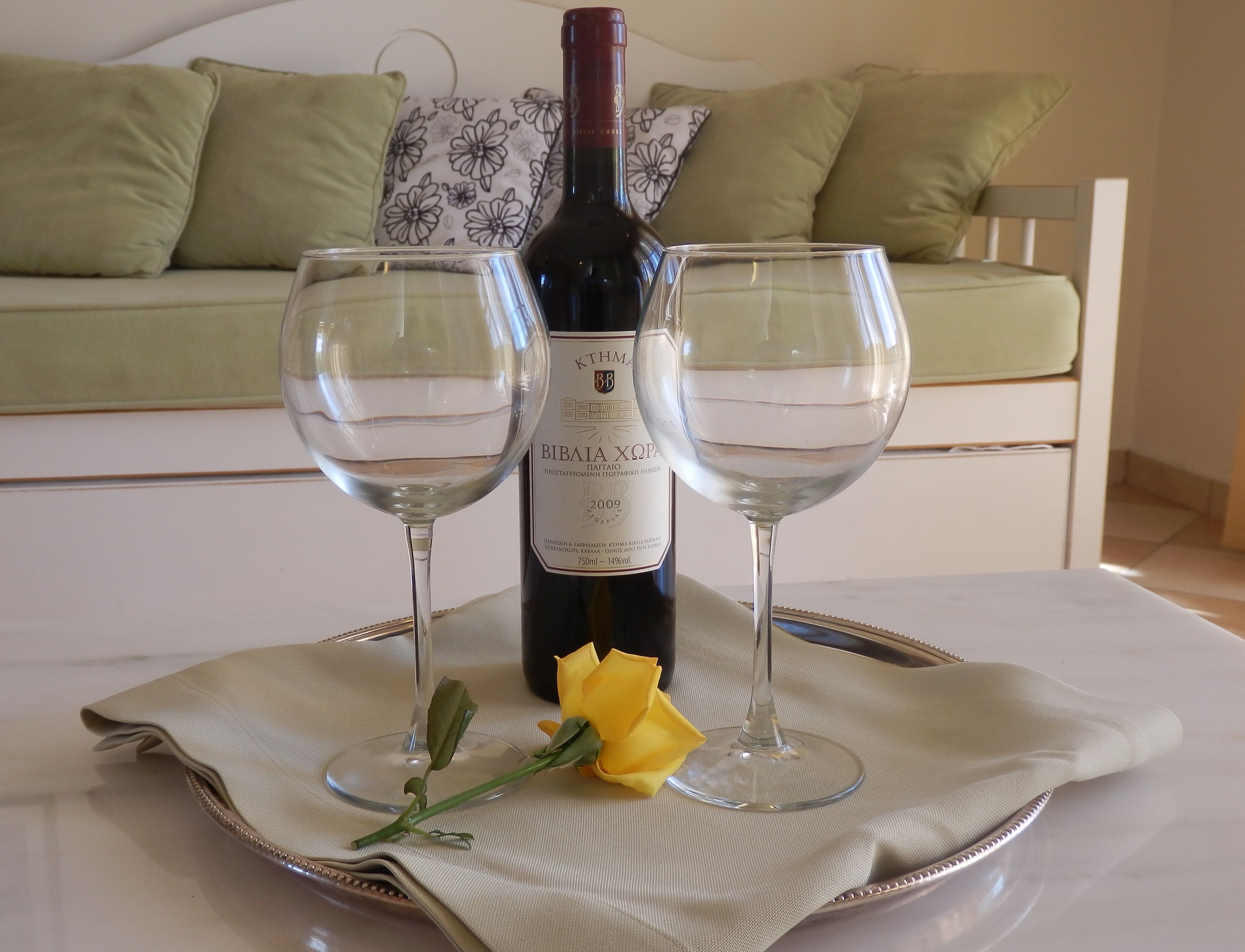 Une bouteille de vin, deux verres à vin vides et une rose jaune sur un plateau.