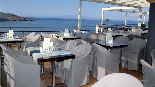 Un área de comedor al aire libre con mesas y sillas, con vista al mar.