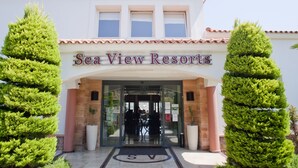 La entrada de Sea View Resorts, con una puerta de vidrio transparente, techo de tejas y dos altos árboles verdes a cada lado.
