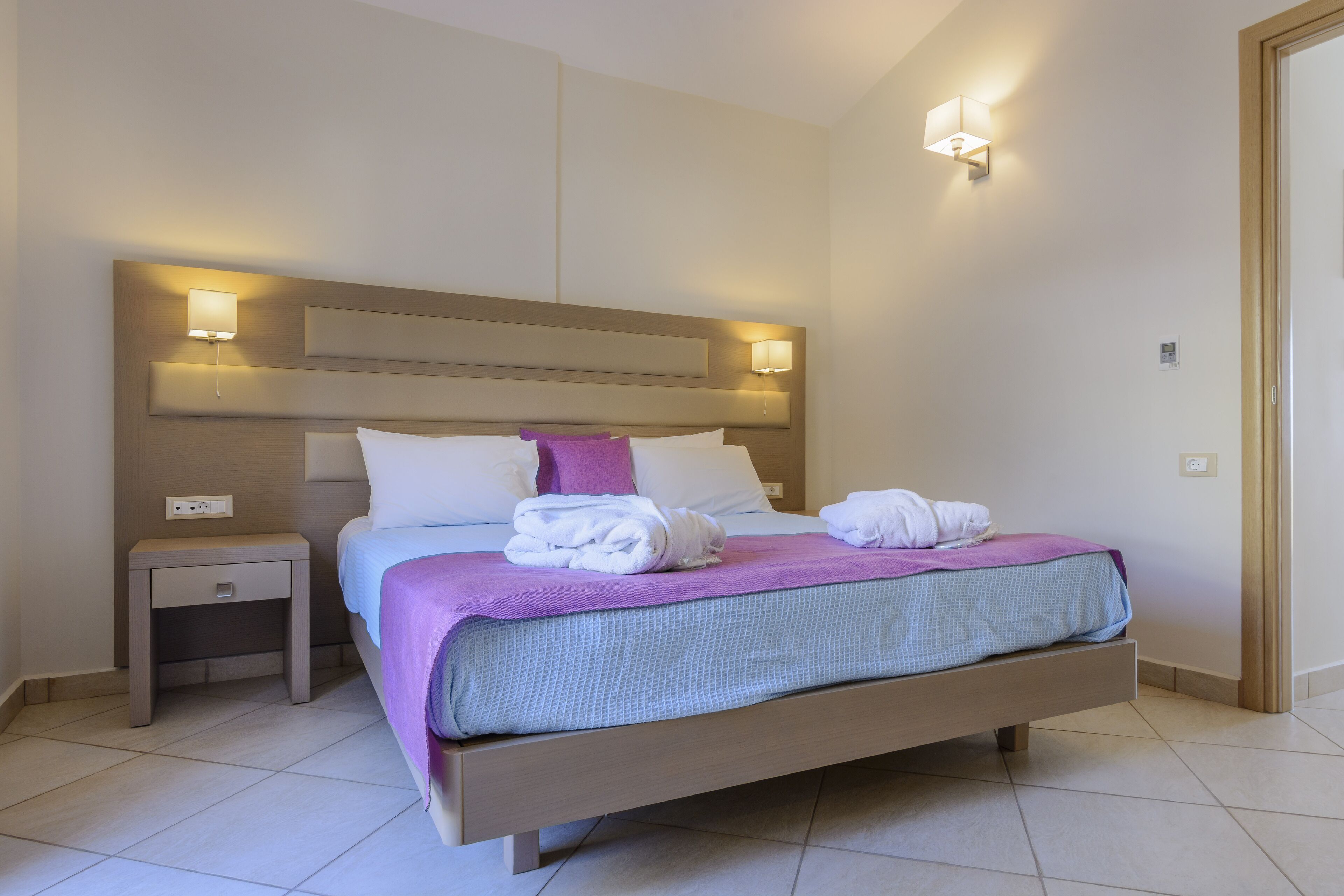 Una habitación de hotel moderna con una cama grande, dos mesitas de noche e iluminación empotrada en la pared.