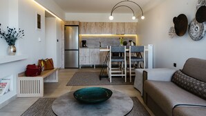Eine moderne Küche mit Holzausstattung, ein Essbereich mit Tisch und Stühlen sowie ein Wohnzimmer mit Sofa und einer dekorativen Schale auf einem runden Tisch.