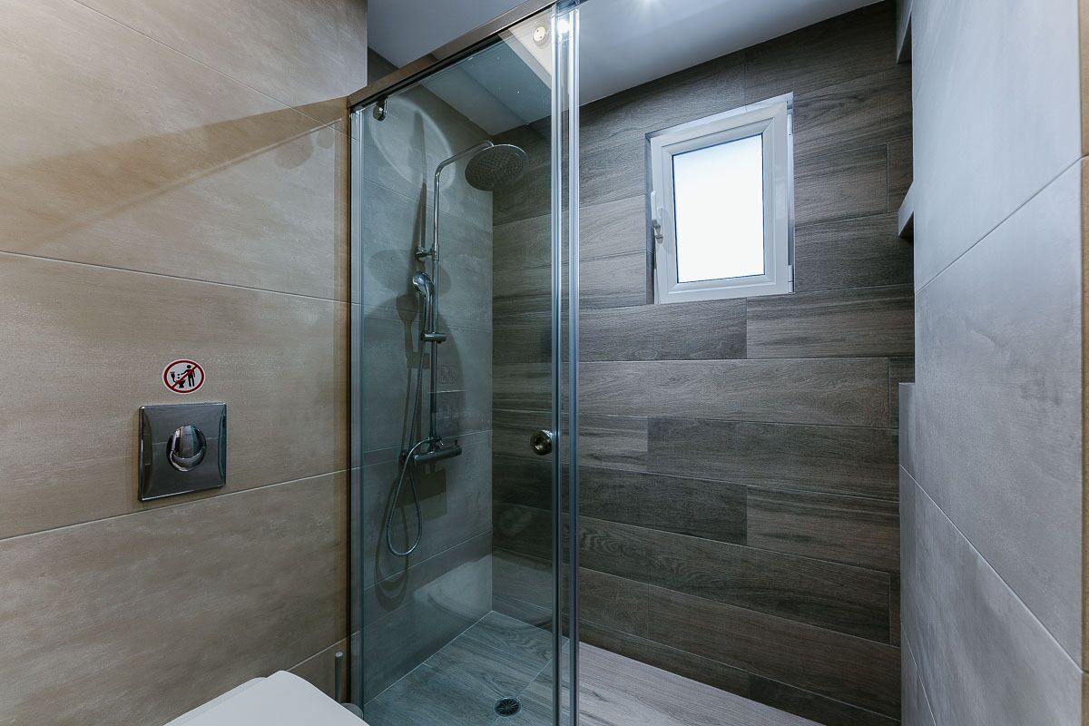 A glass-enclosed shower with a showerhead and handheld shower attachment, a small window, and a wall-mounted control panel.