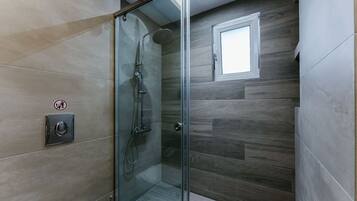 A glass-enclosed shower with a showerhead and handheld shower attachment, a small window, and a wall-mounted control panel.