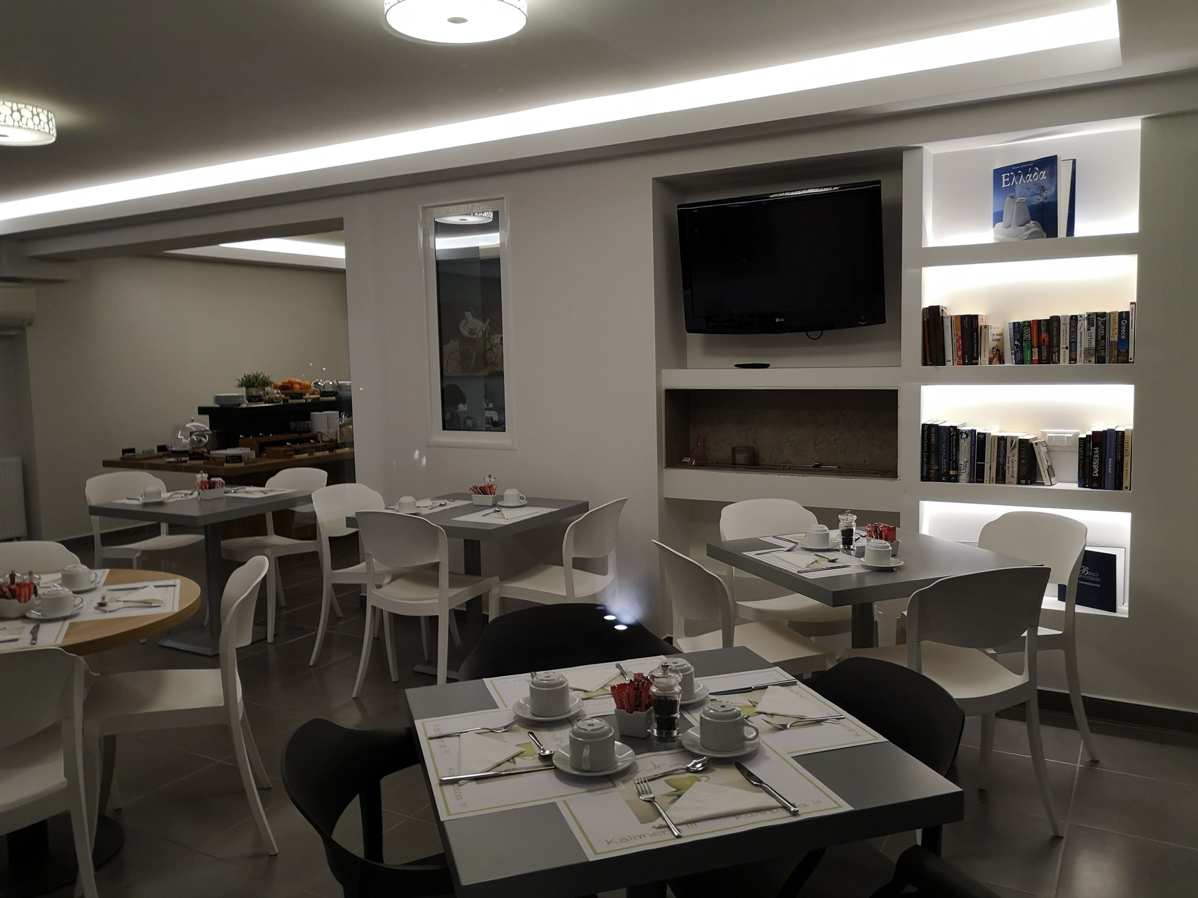 A modern dining area with tables set for four, white chairs, and a flat-screen TV mounted on the wall.
