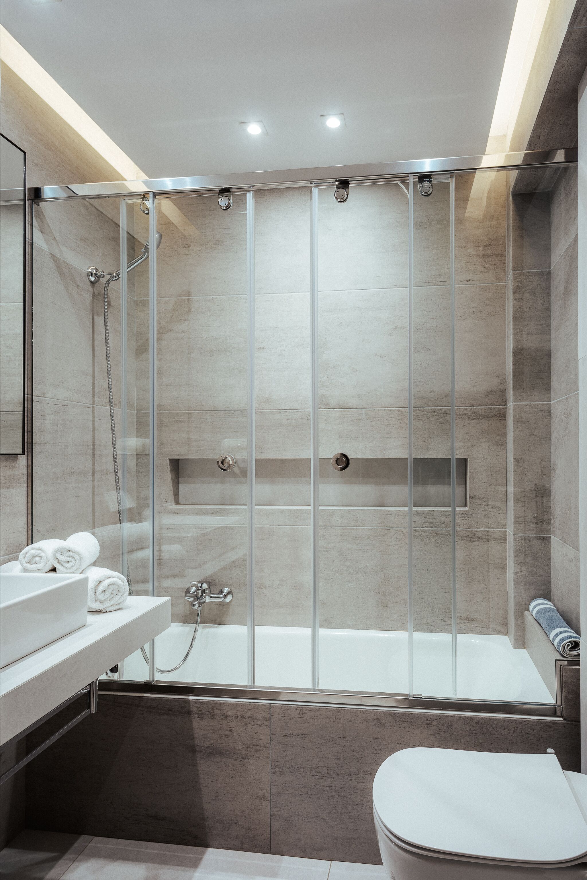 A modern bathroom with a glass-enclosed shower, a white bathtub, and a toilet.