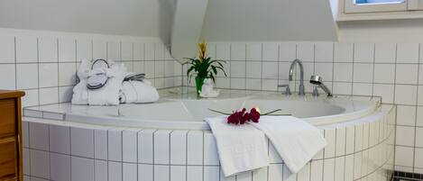 A modern bathroom with a large bathtub, white tiles, a wooden cabinet, and a potted plant.