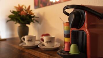 A coffee machine with a red body and a black handle, a green cup, and a white cup with a saucer on a wooden table.