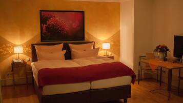 Habitación de hotel con una cama grande, dos mesitas de noche con lámparas, una mesita pequeña con un florero y un cuadro en la pared.