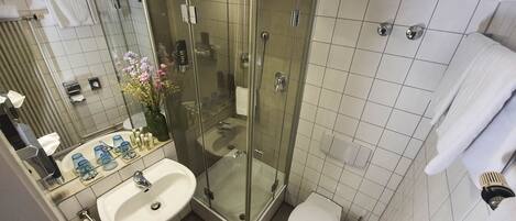 Ett modernt badrum med en dusch som är avskärmad med glasväggar, ett vitt handfat och en toalett.
