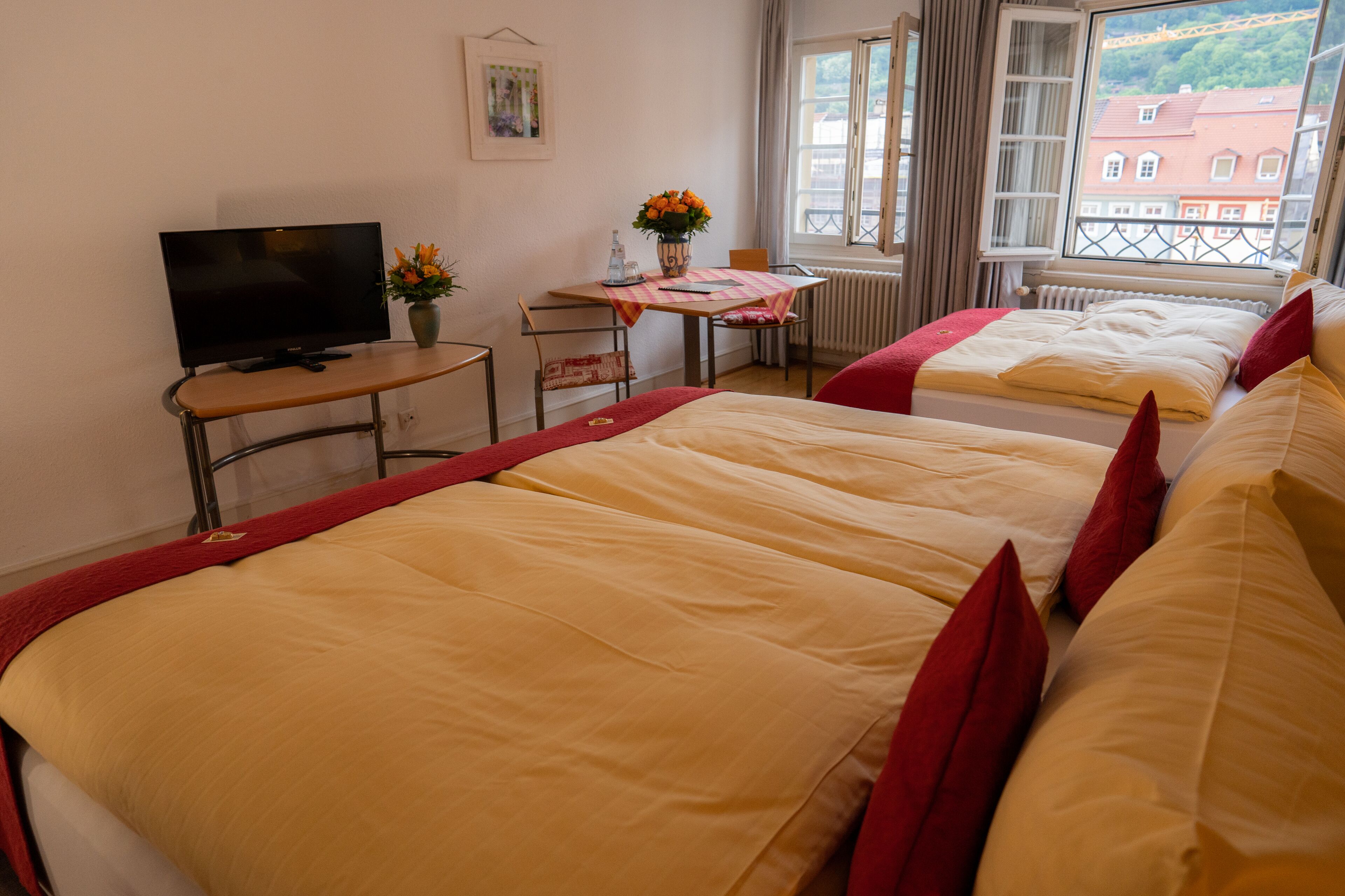 Habitación de hotel con dos camas, un televisor, una mesita con un florero y una ventana que ofrece vistas a edificios.