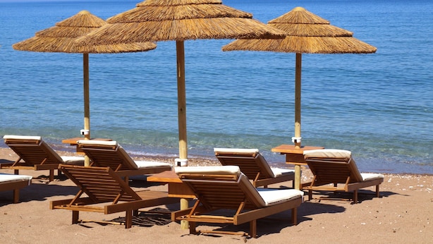 A beach with wooden lounge chairs and thatched umbrellas. - Messina Resort Hotel (Trifylia)