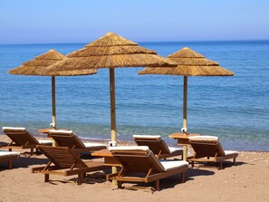 A beach with wooden lounge chairs and thatched umbrellas.