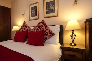 A hotel room with a bed, two red and white patterned pillows, a bedside lamp, and two framed pictures on the wall. - Dunhallin House (Inverness)