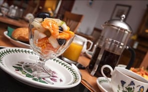 A breakfast setting with a fruit bowl, a coffee pot, and a cup of coffee on a table. - Dunhallin House (Inverness)