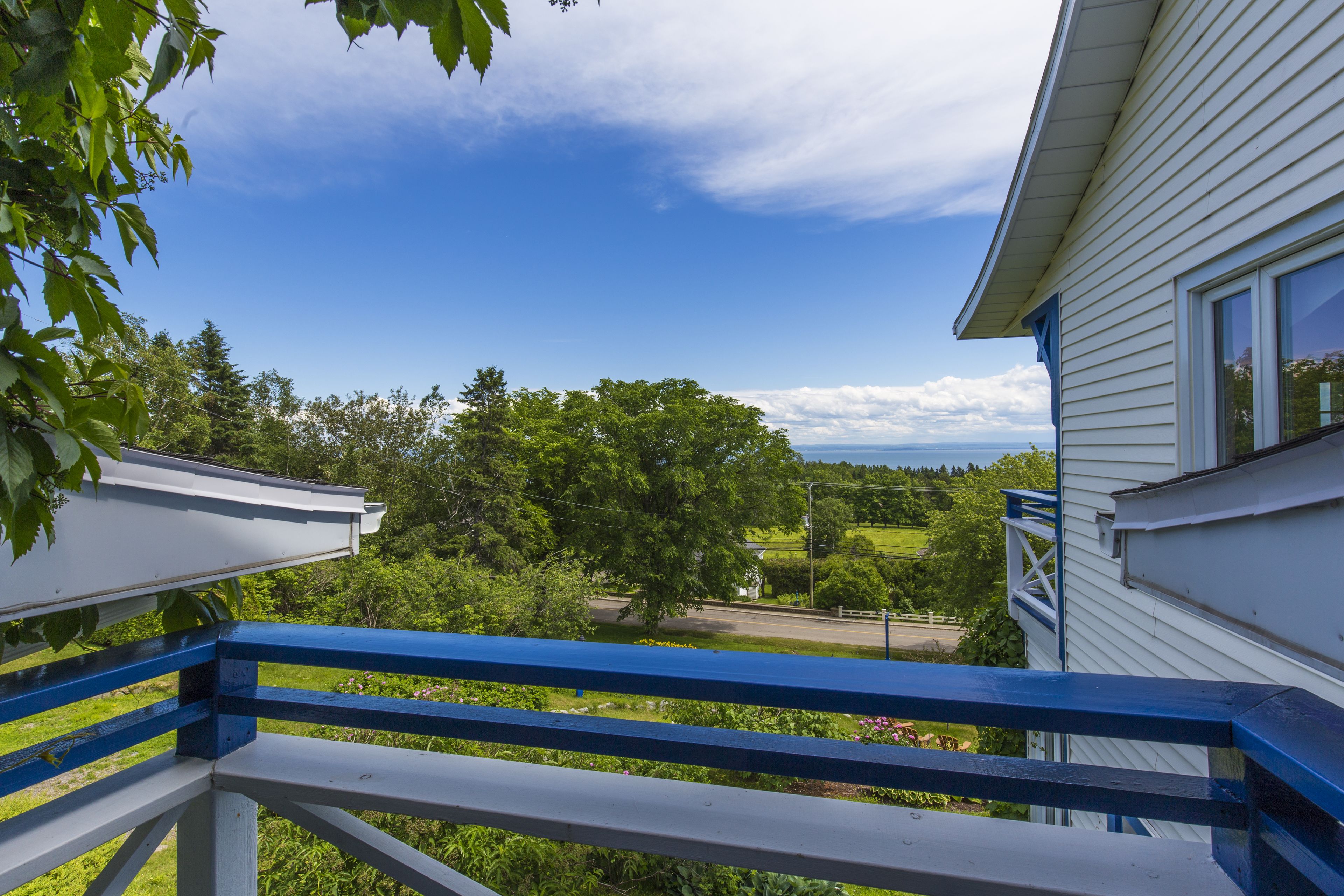 Un balcone con ringhiera blu affaccia su un paesaggio verde e un edificio bianco.