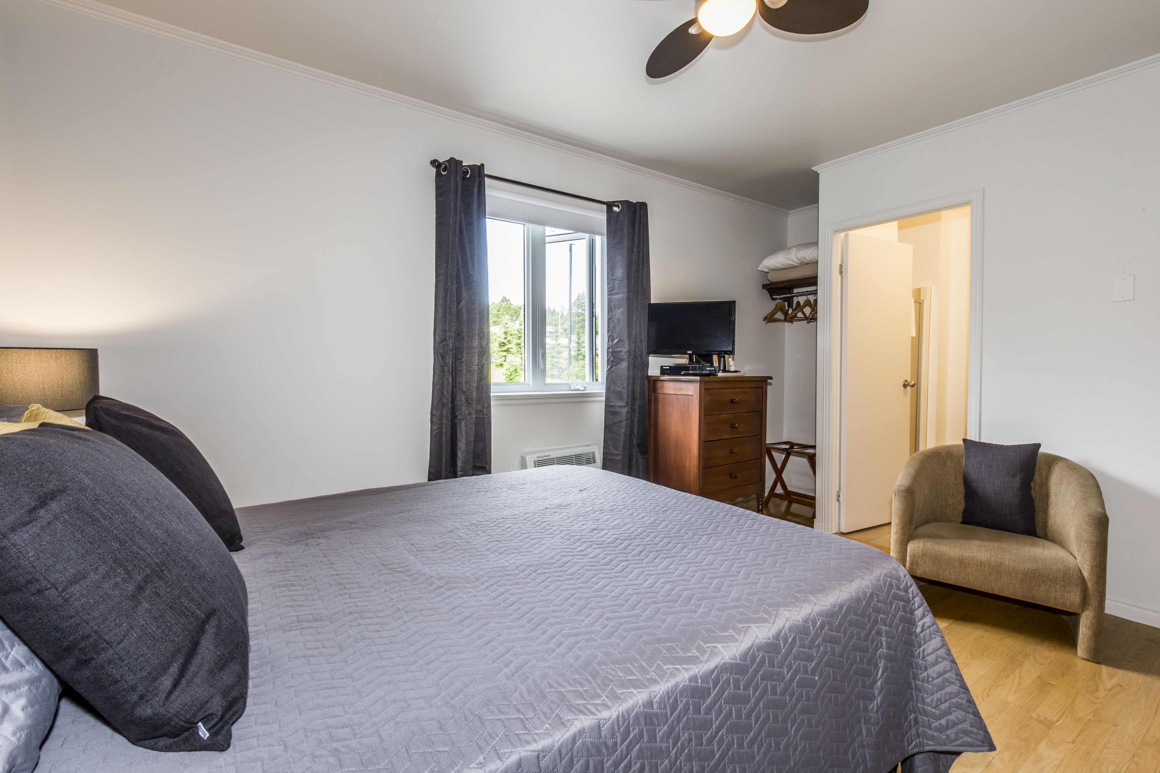 A bedroom with a bed, a chair, a desk, and a window.