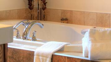 A bathroom with a large bathtub, a double sink, and decorative plants.