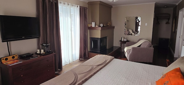 A hotel room with a bed, a TV, a desk with a computer, a fireplace, and a mirror. - Auberge Fleurs de Lune (La Malbaie)