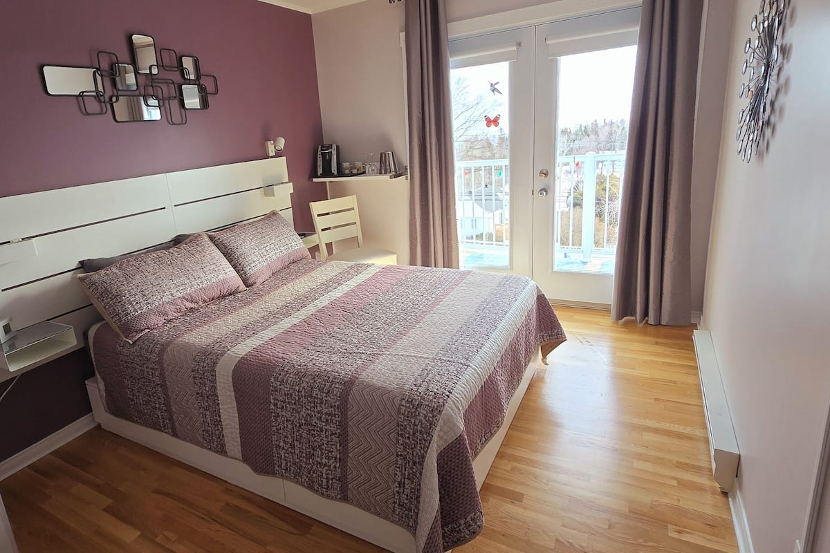 Un dormitorio con cama, mesitas de noche, un espejo en la pared y un balcón con vistas.