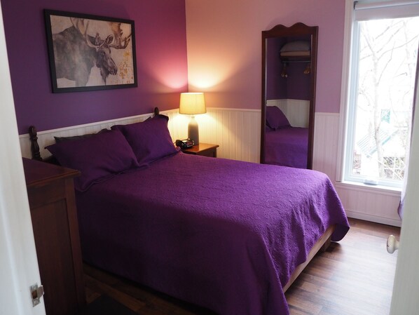 Un dormitorio con una cama, una mesita de noche, una lámpara, un espejo y una ventana.