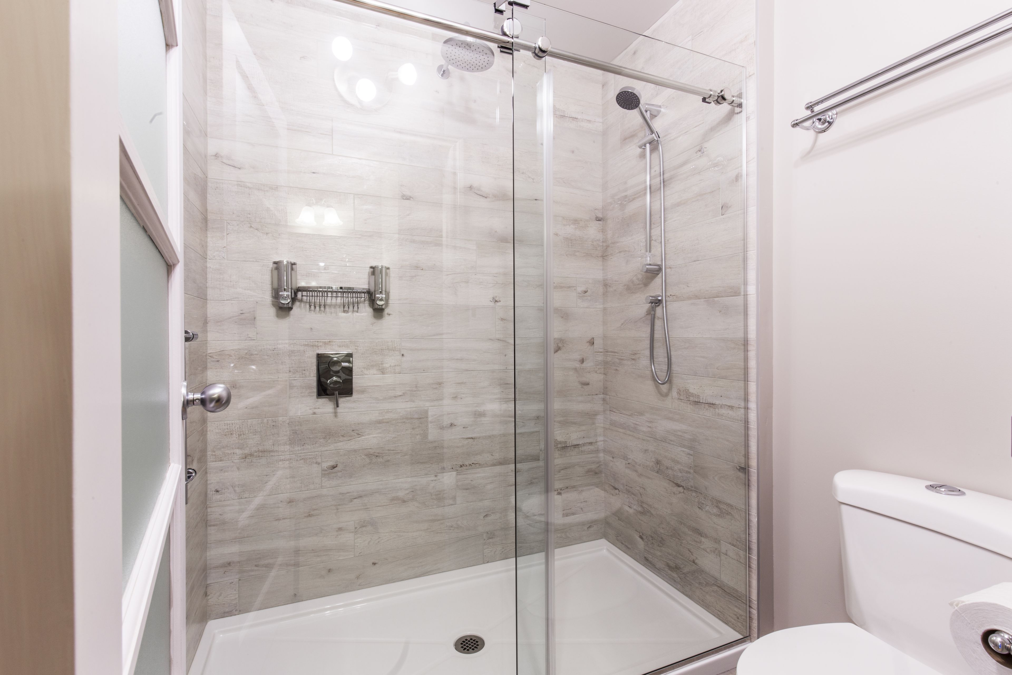 A modern bathroom with a glass-enclosed shower, a toilet, and a glass door.