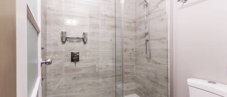 A modern bathroom with a glass-enclosed shower, a toilet, and a glass door.