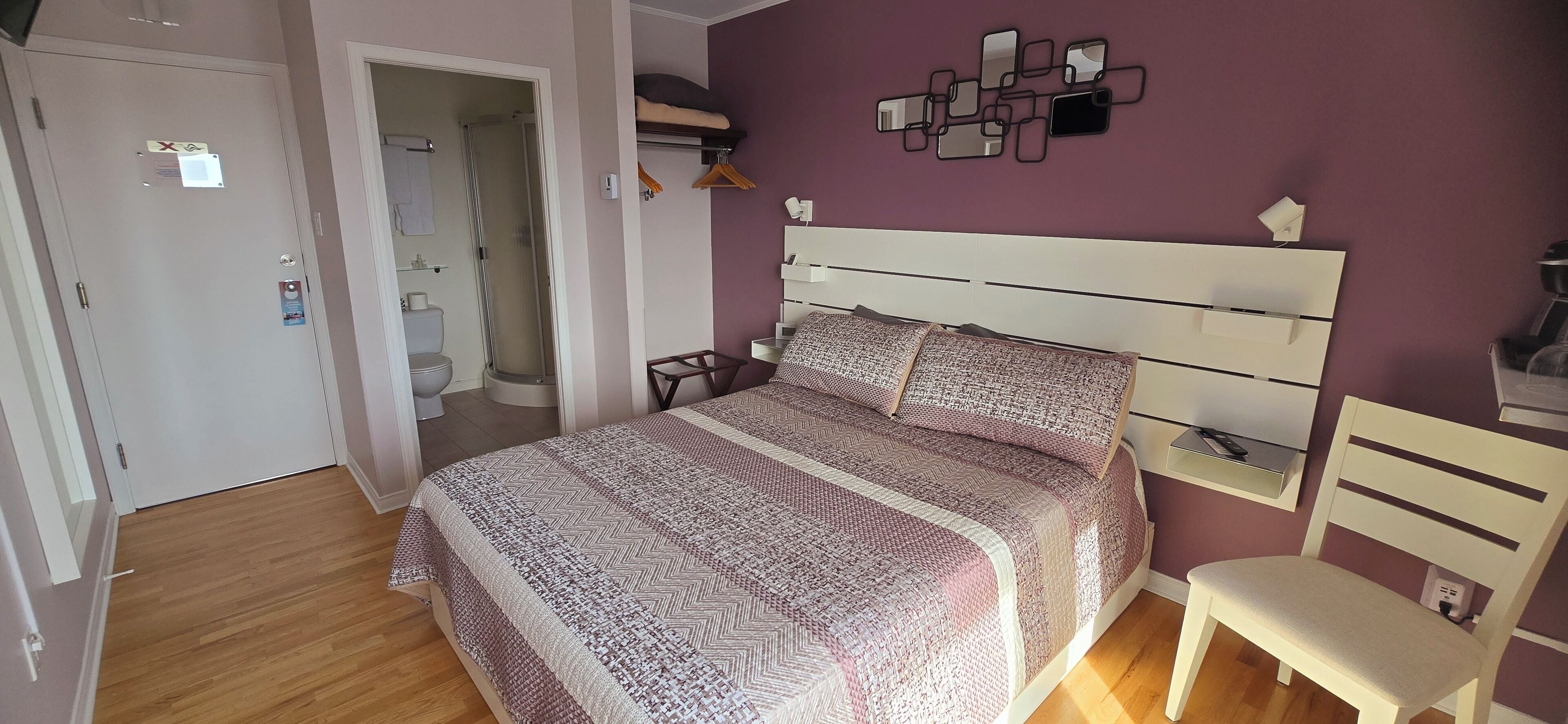 A bedroom with a bed, a chair, a bedside table, and a wall-mounted mirror.