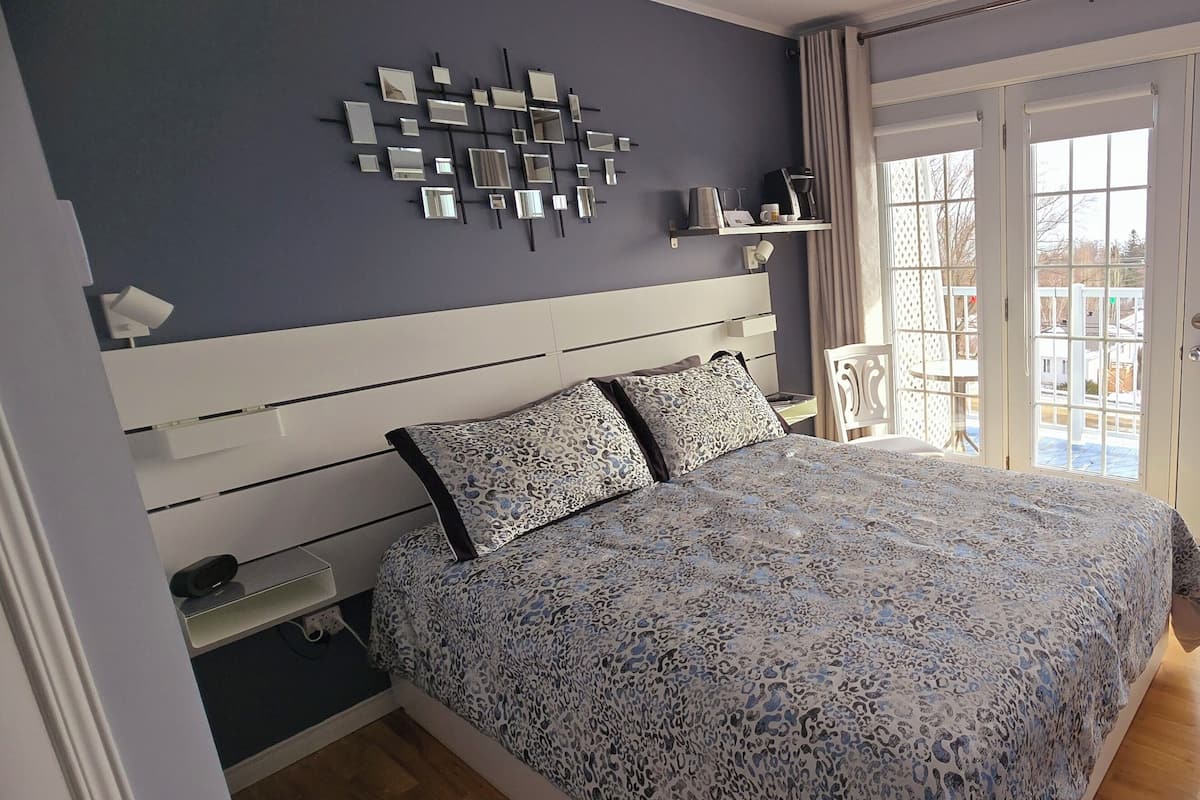Un dormitorio con cama, mesitas de noche, un espejo en la pared y vistas a través de un ventanal.