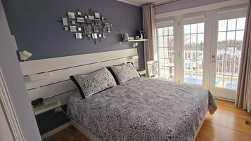 Un dormitorio con cama, mesitas de noche, un espejo en la pared y vistas a través de un ventanal.