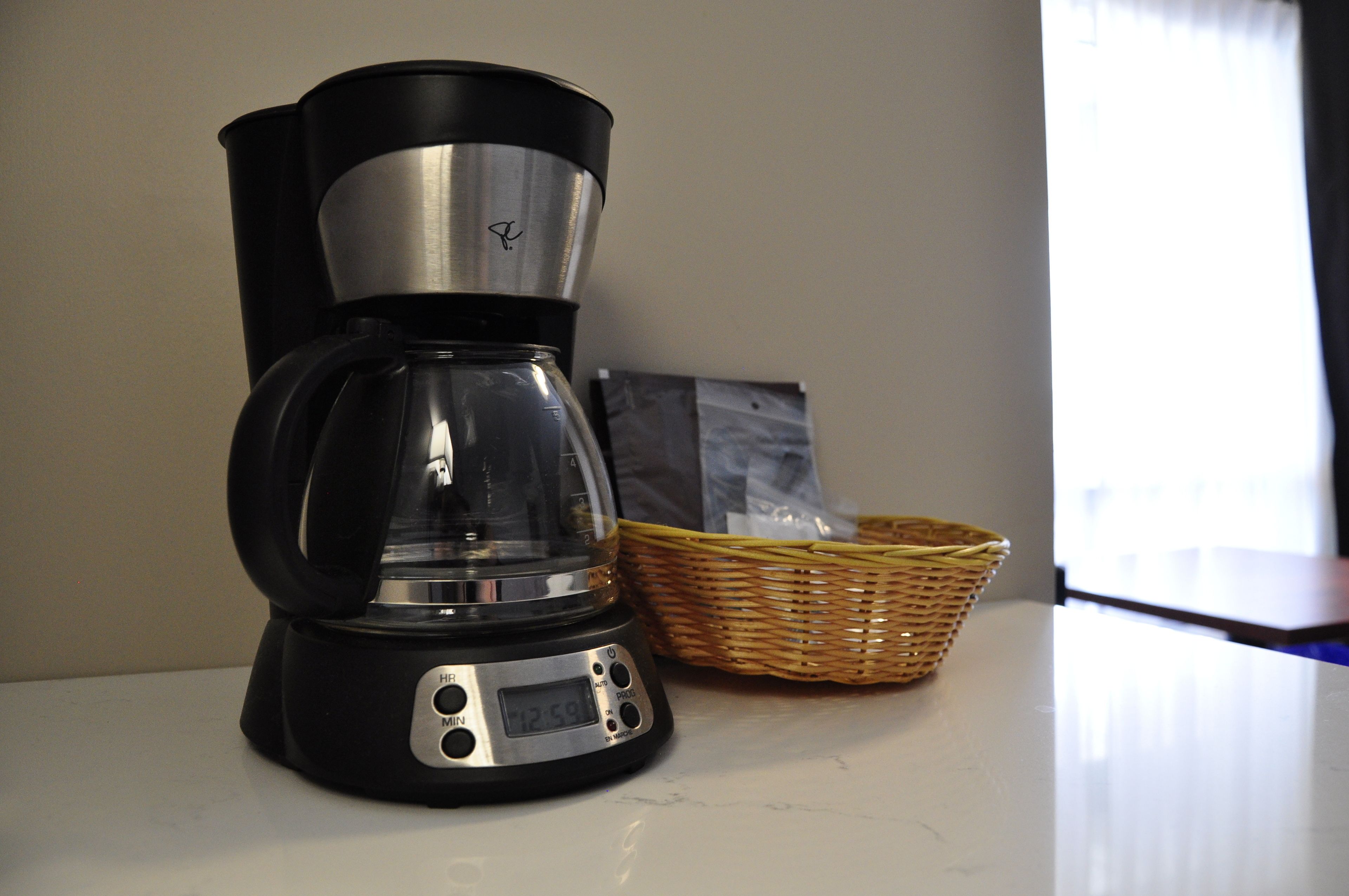 A coffee maker on a countertop with a basket and a bag in the background.