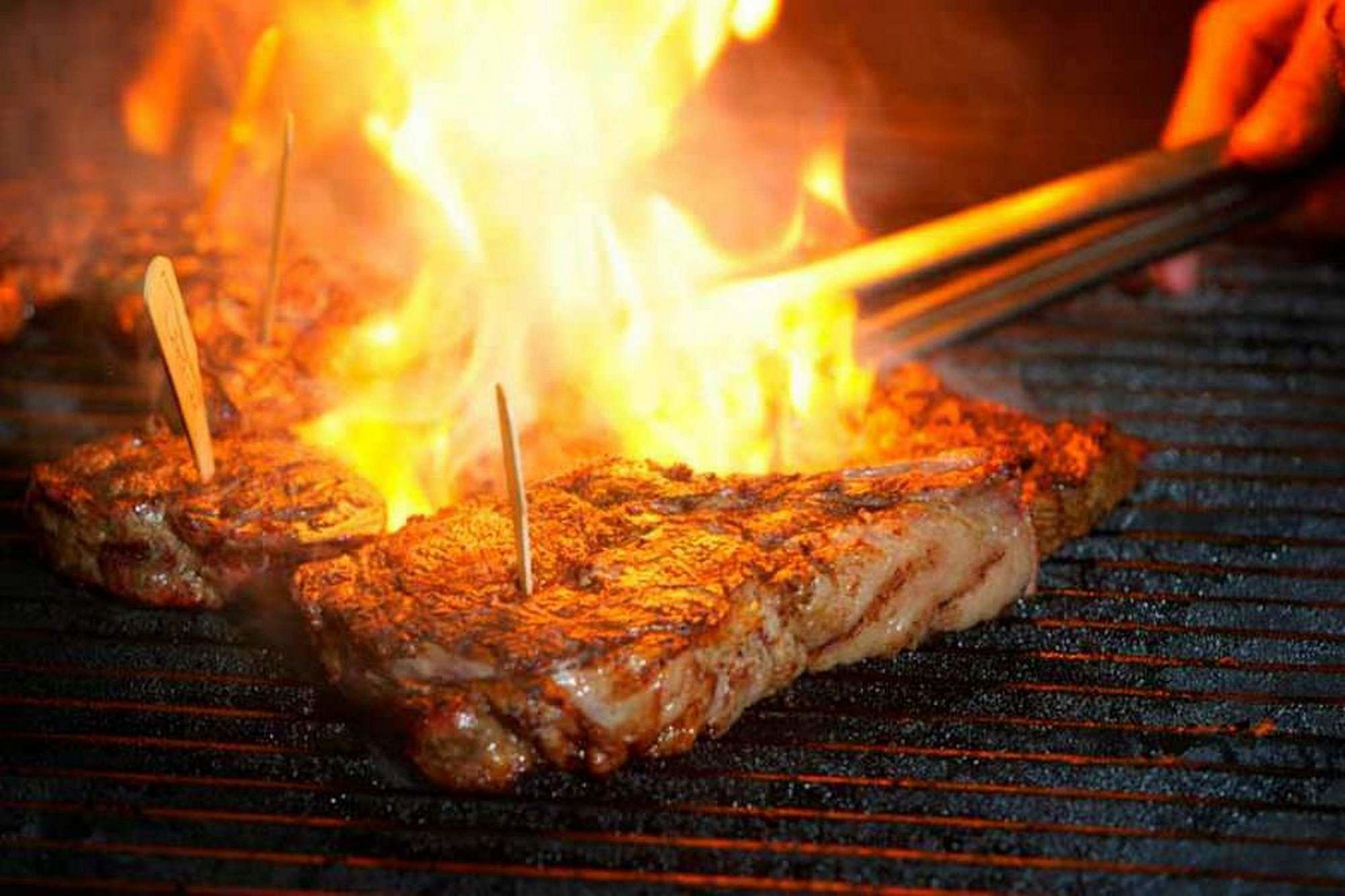 Steaks werden über offene Flammen gegrillt, dazu werden Zangen benutzt.