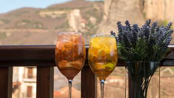 Two glasses of beverages on a balcony with a view of a mountain and a cliff.