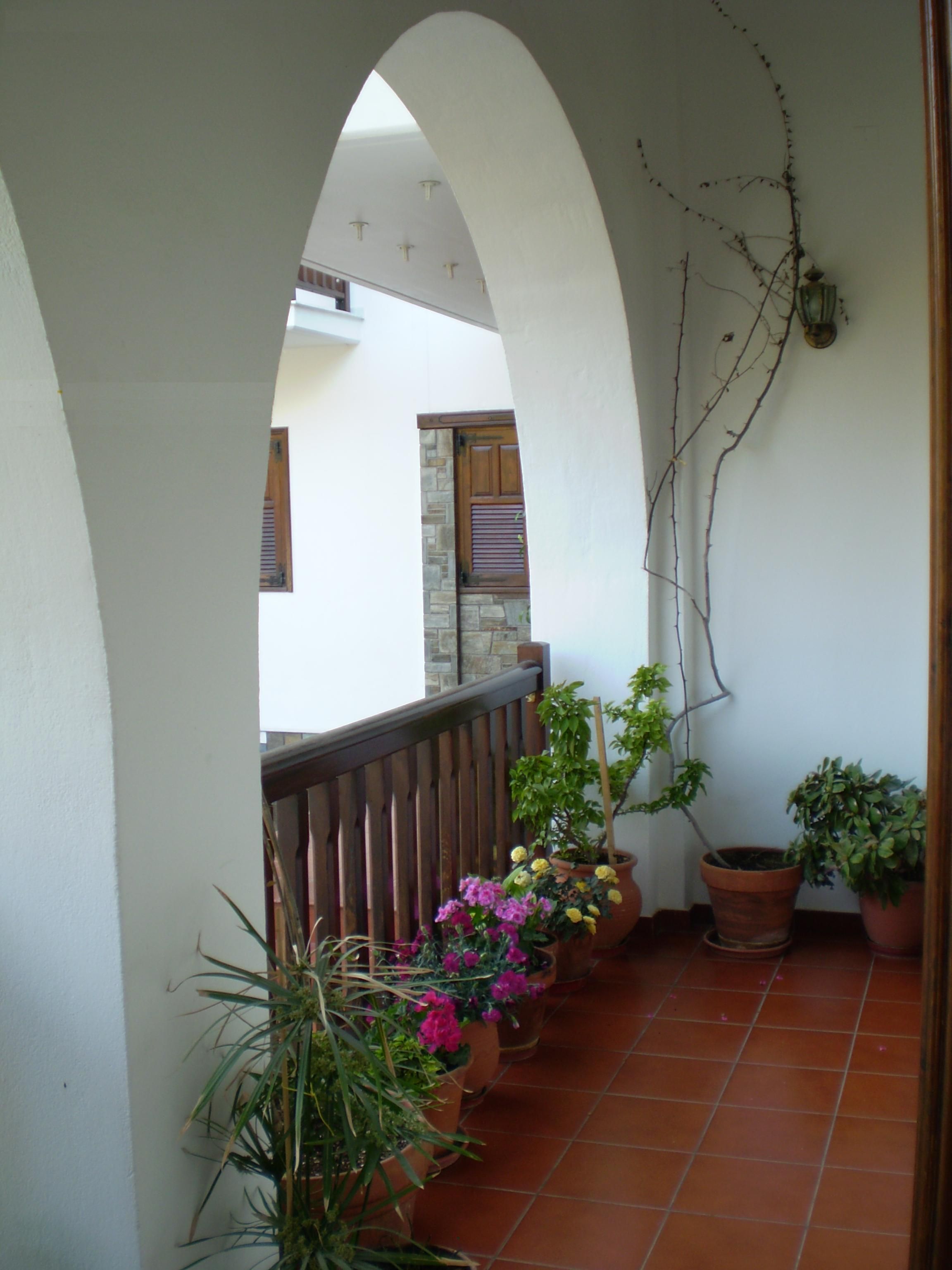 A covered balcony with terracotta tiles, potted plants, and a wooden railing.