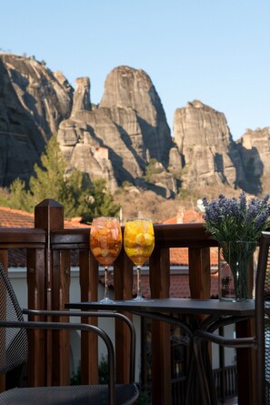 A balcony with a view of rock formations, a wooden railing, and a table with two glasses of drinks and a vase of flowers. - Hotel Kastraki (Kalabaka)