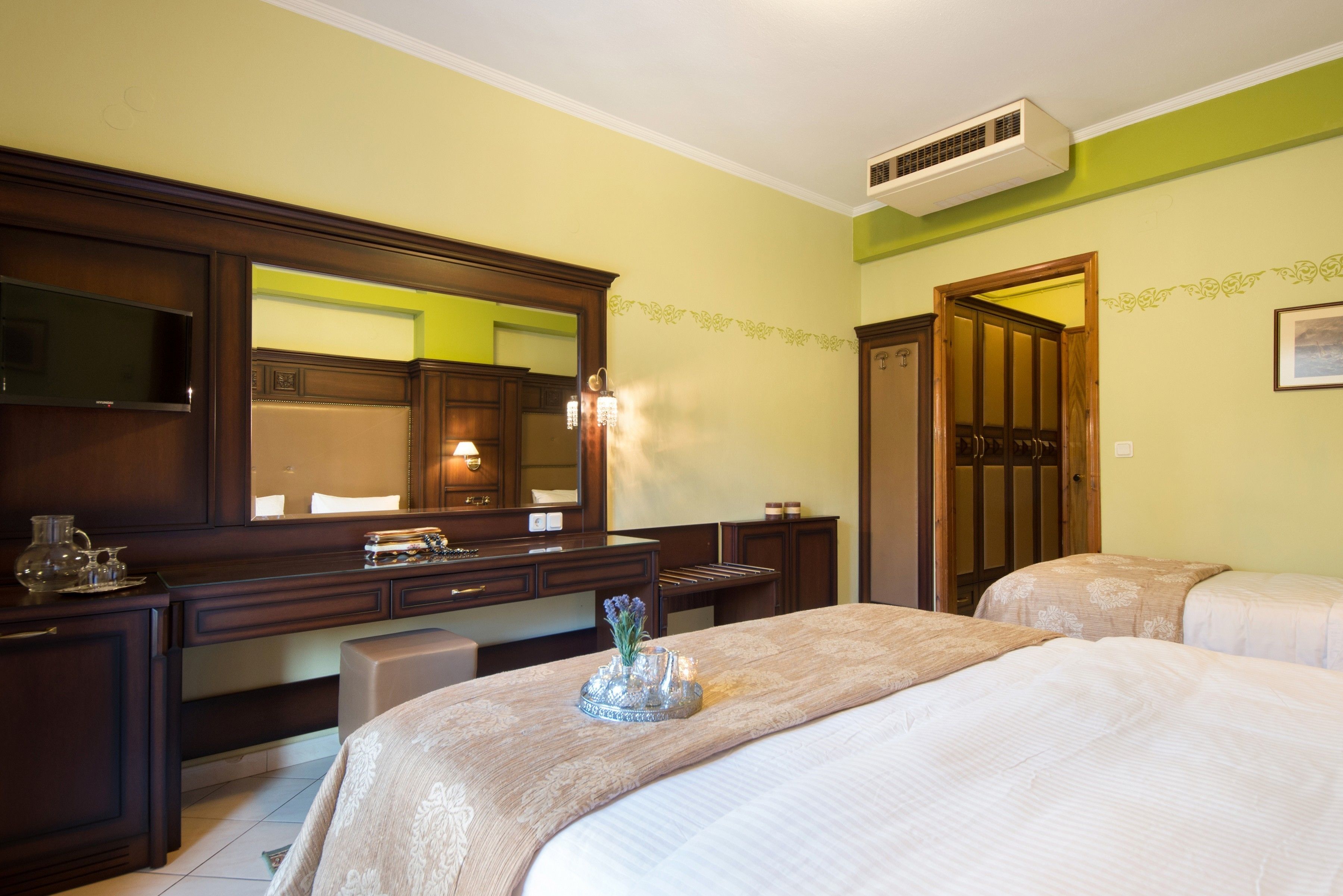 A hotel room with a large bed, a bedside table, a dresser, a mirror, and a door leading to another room.