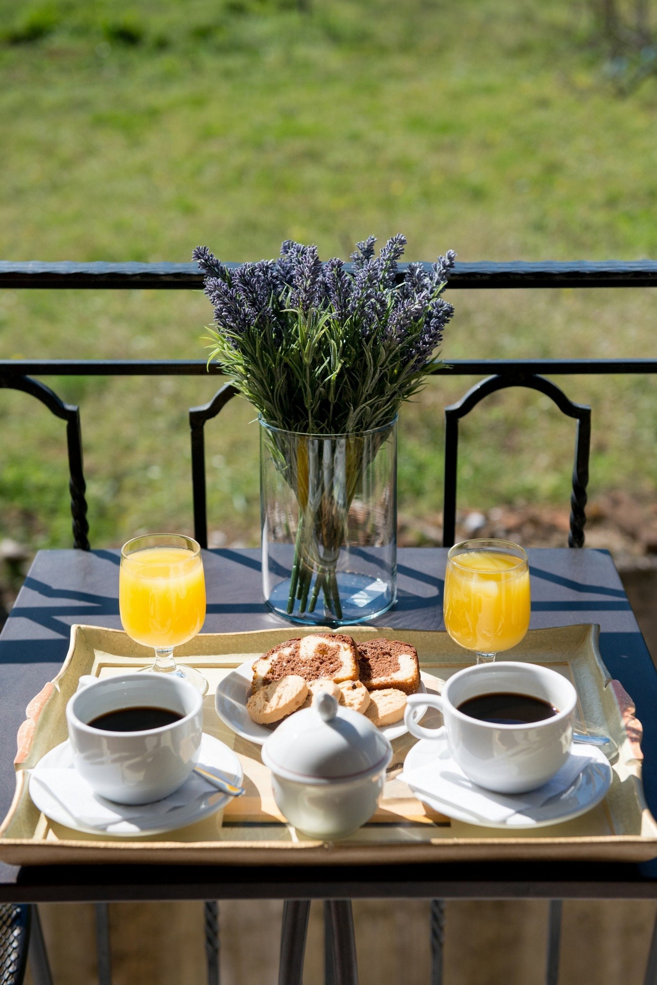 A tray with breakfast items including coffee, tea, toast, and juice, placed on a table with a view of a grassy area.