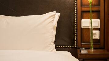 A neatly made bed with white linens, a bedside table with a lamp, and a vase with a single white flower.