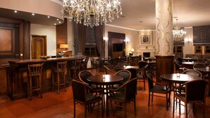 A spacious hotel lobby with a bar area, multiple dining tables, and elegant chandeliers. - Hotel Kastraki (Kalabaka)