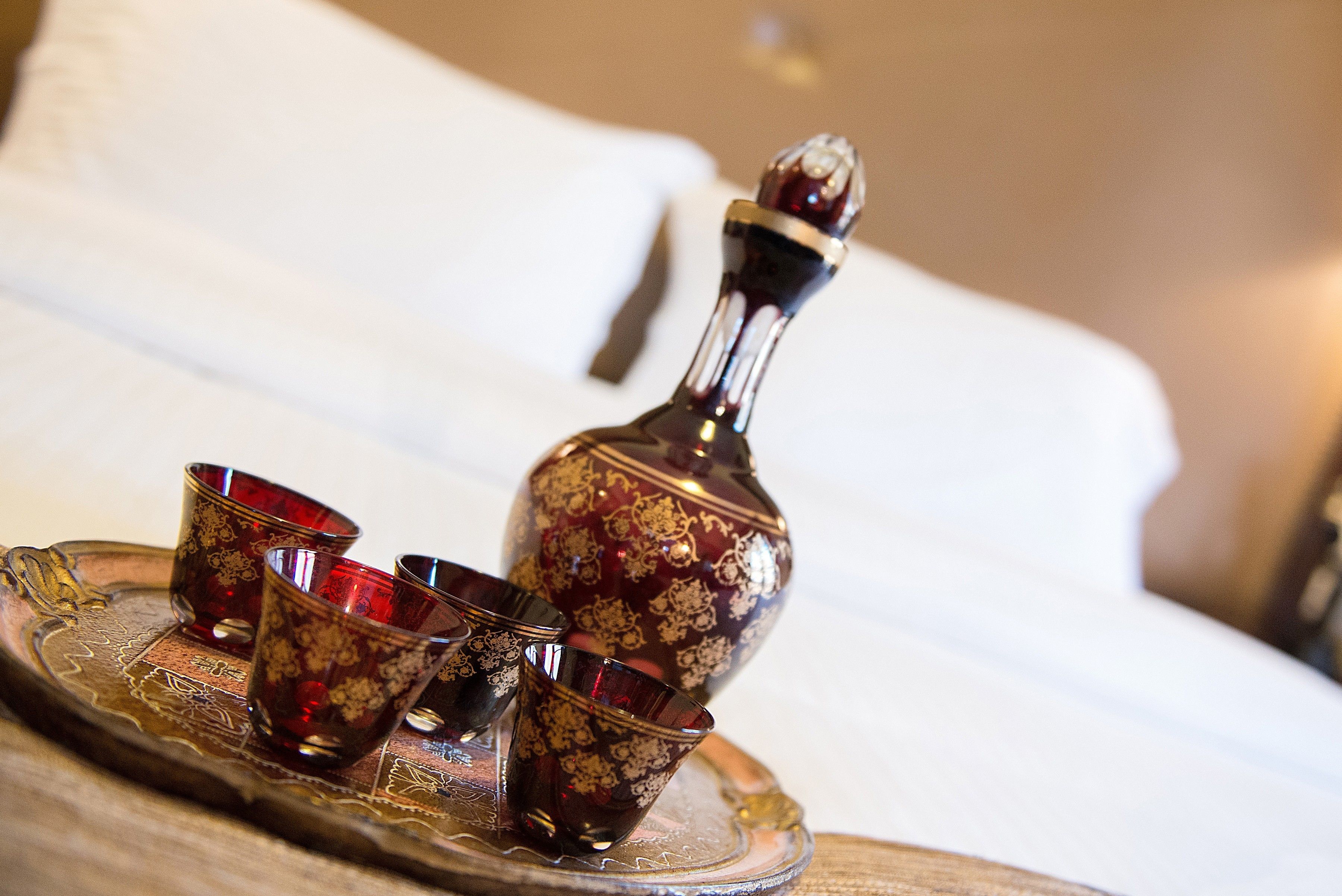 Un plateau avec une bouteille décorative et trois verres, le tout posé sur un lit.