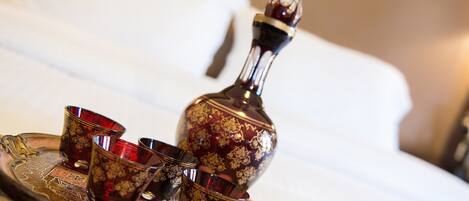 Una bandeja con una botella decorativa y tres vasos sobre una cama.