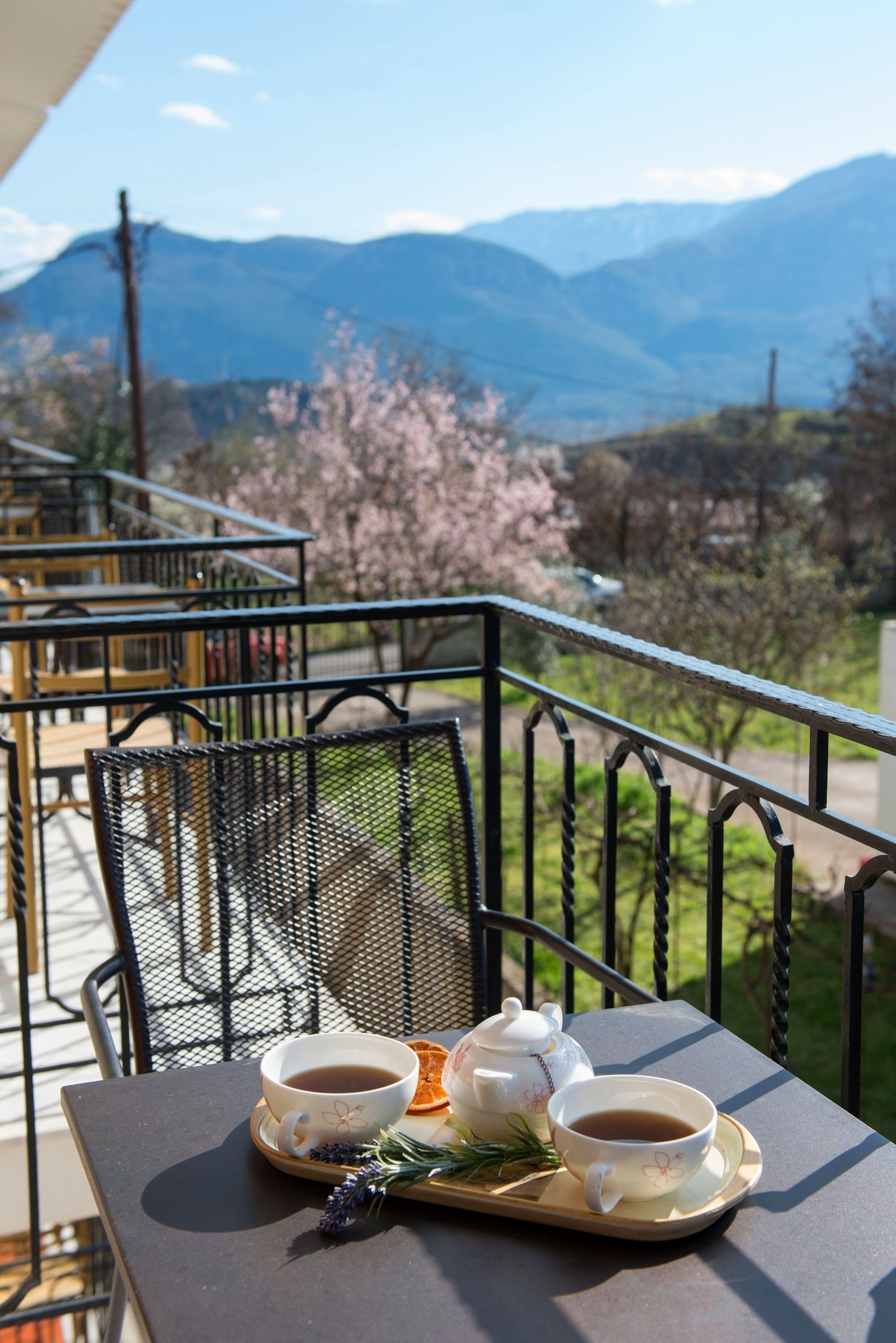 Un balcon avec une table dressée pour le thé, donnant sur un paysage montagneux où les arbres sont en fleurs.